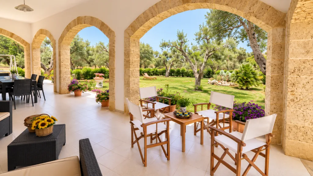 Portico con divani, tavolo da pranzo e vista sul giardino di ulivi